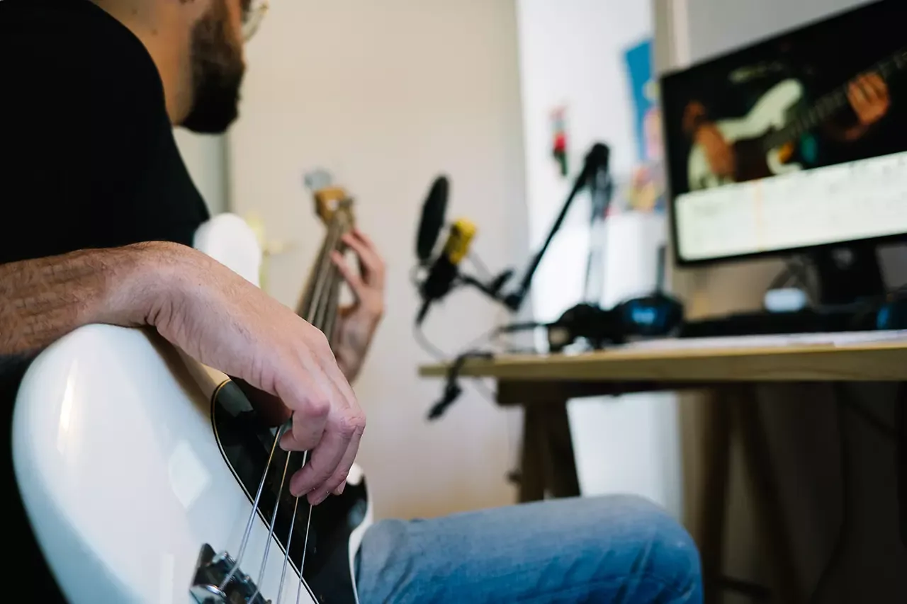 A musician practicing bass guitar during an online lesson.