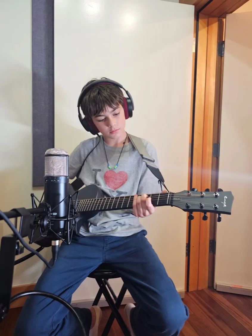 A student recording acoustic guitar in a recording booth