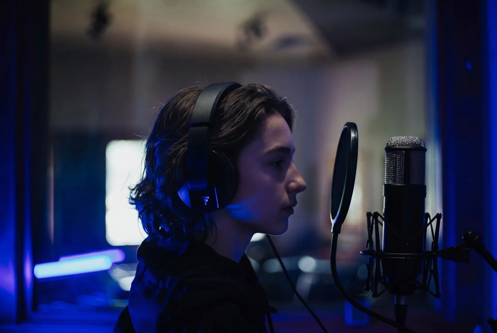 A teenager singing into a studio microphone in blue light during a recording session