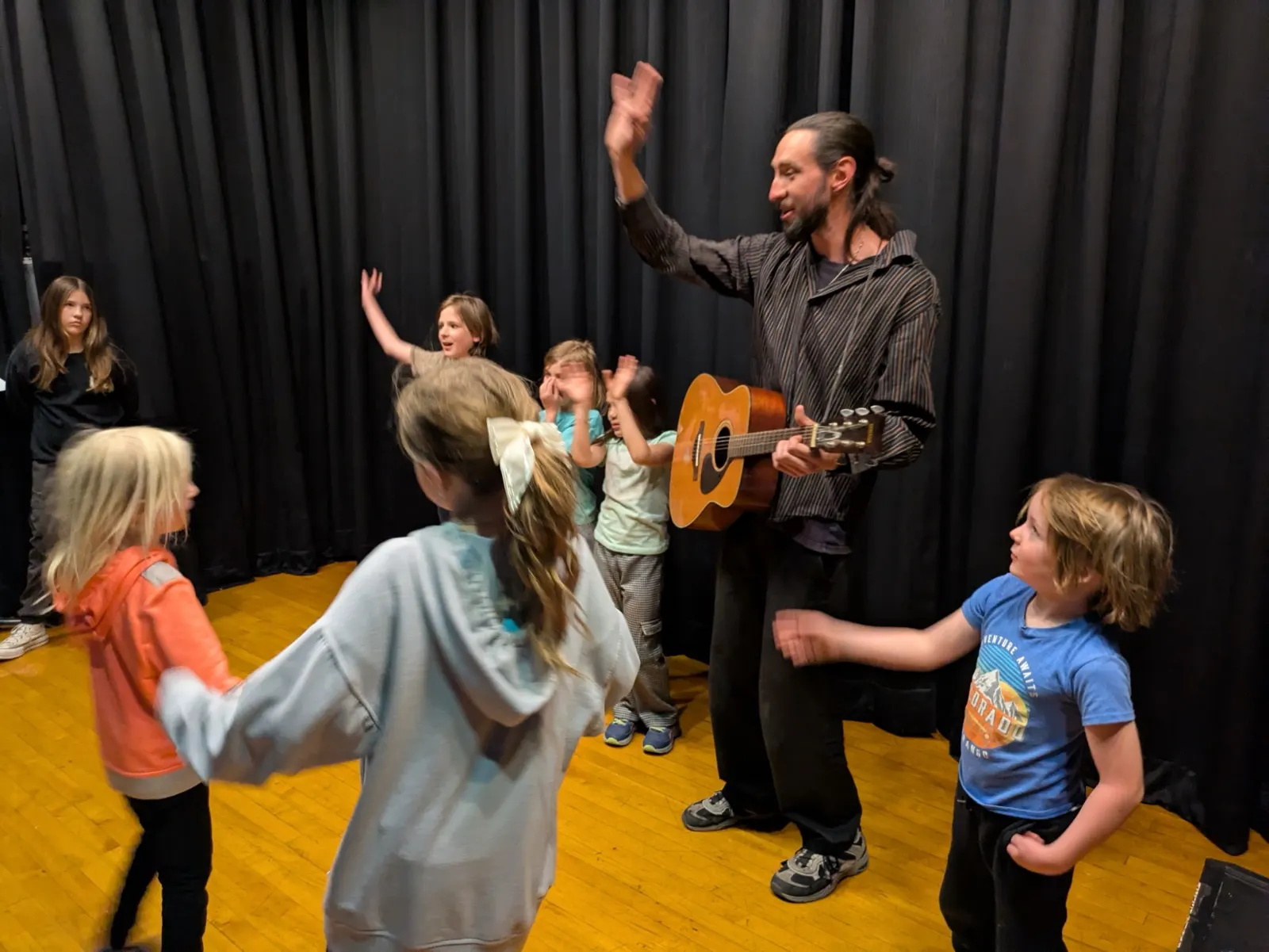 Children dancing around their teacher as he plays guitar