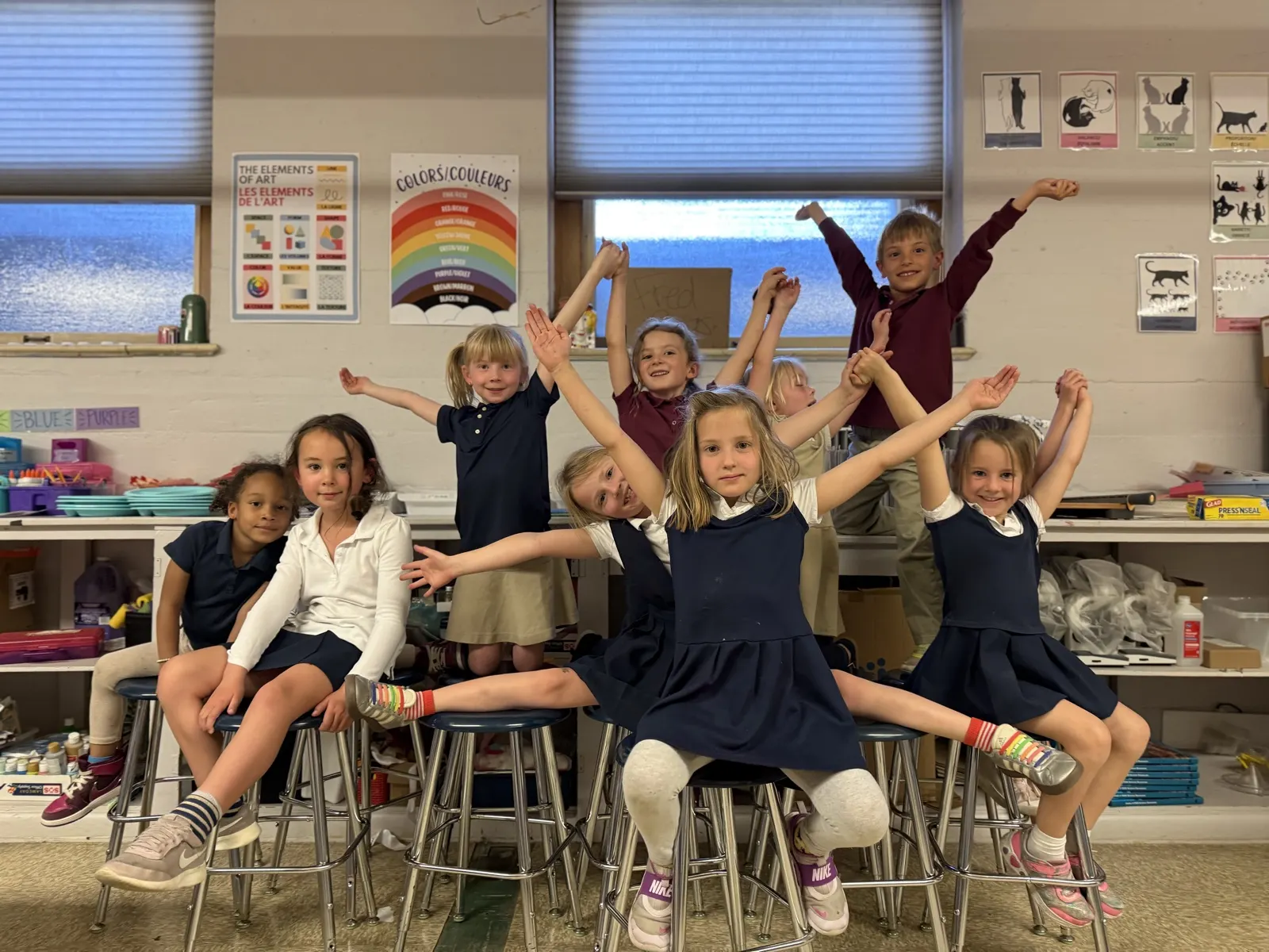 A class of young students in school uniforms cheering with their arms in the air