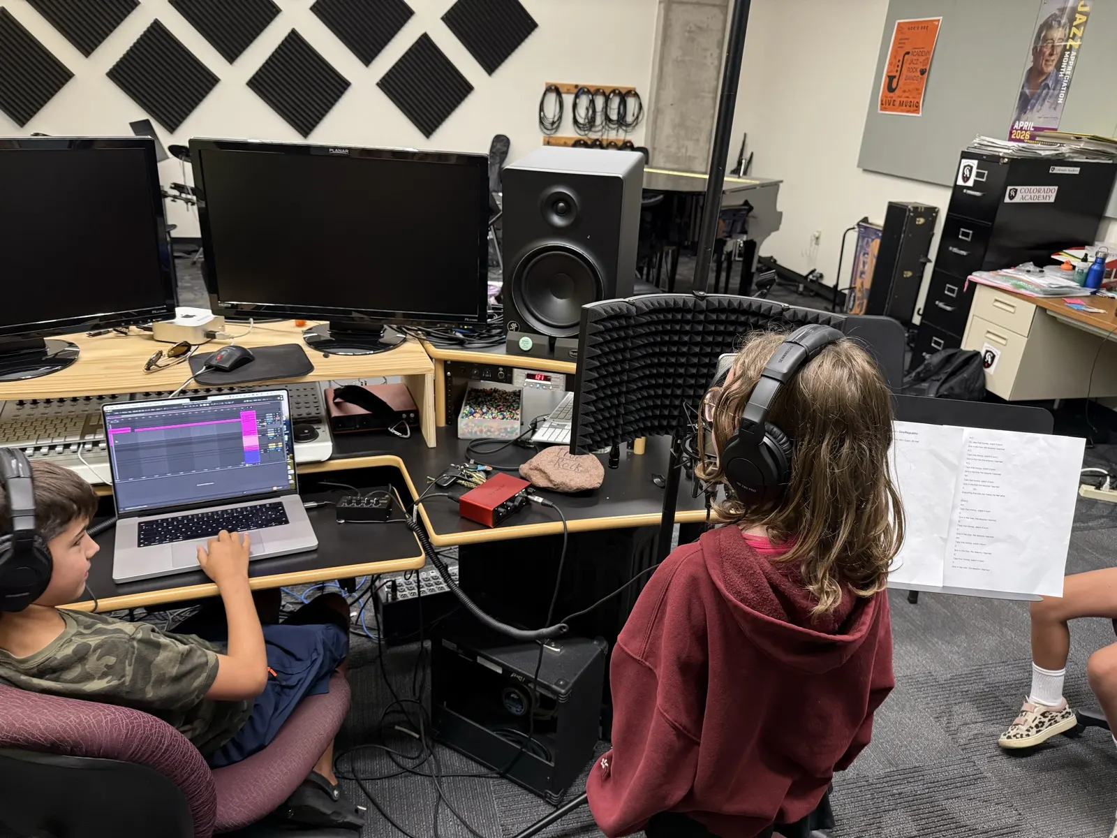 A student singing at the microphone while a classmate runs the recording on a laptop