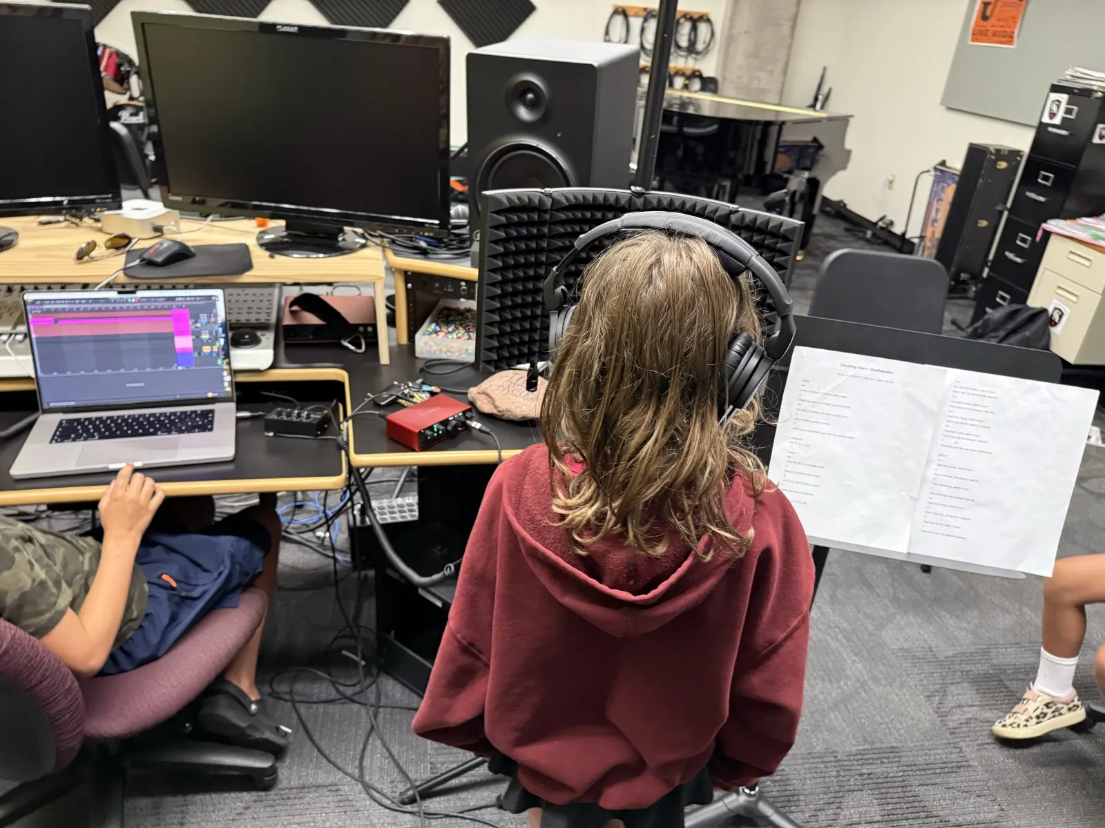 A student in headphones reading a lyric sheet at the microphone