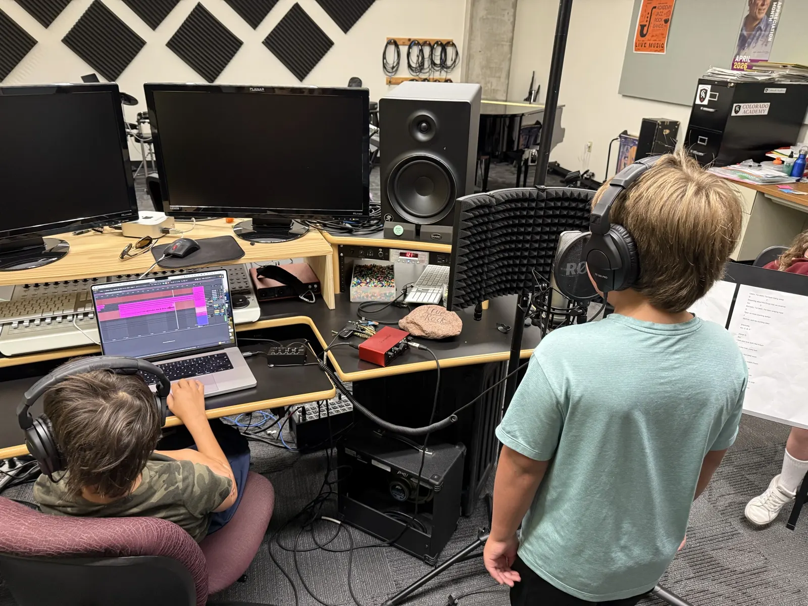 Two students recording a song, one at the microphone and one at the laptop